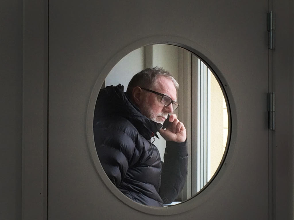 Stefan Nolervik i telefon, sedd genom ett runt fönster i en dörr
